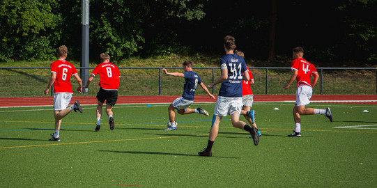 Foto: Ein Fußballteam in blauen Trikots und ein Fußballteam in roten Trikots spielen auf einem Fußballfeld gegeneinander.