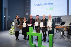 People with certificates behind the TU logo at the academic anniversary celebration of TU Dortmund University.