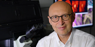 Porträtfoto von Stefan W. Hell mit Mikroskop im Hintergrund