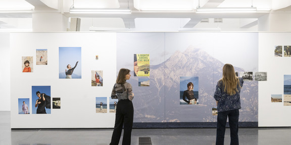 Zwei Frauen betrachten die Fotos einer Ausstellung, sie stehen mit dem Rücken zur Kamera.