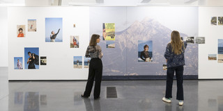 Zwei Frauen betrachten die Fotos einer Ausstellung, sie stehen mit dem Rücken zur Kamera.