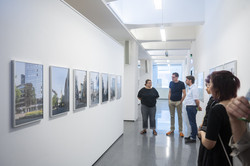 Links Architekturfotografien in einem Ausstellungsflur. Rechts eine Personengruppe, die sich die Fotografien ansieht.