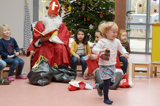 Ein als Nikolaus verkleideter Mann verteilt Geschenke an Kindergartenkinder.