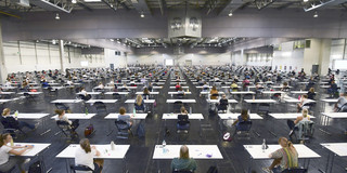 Students sit spaced apart at tables in the Westfalenhalle to write an exam.