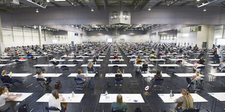 Studierende sitzen mit Abstand an Tischen in der Westfalenhalle, um eine Klausur zu schreiben.