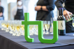 Das TU-Logo steht auf einem Tisch vor gefüllten Sektgläsern.