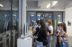 Ausstellung „Rundgang Kunst“ Mehrere Personen stehen an hohen Tisch mit weißem Laken, die an einer Fensterfront stehen.