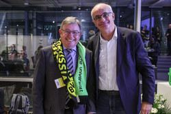 Foto: Zwei Personen stehen nebeneinander, eine trägt einen schwarz-gelb-grünen Schal mit der Aufschrift „Borussia Dortmund“ und „Technische Universität Dortmund“.