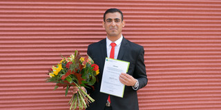 A man holds flowers and a certificate in his hands