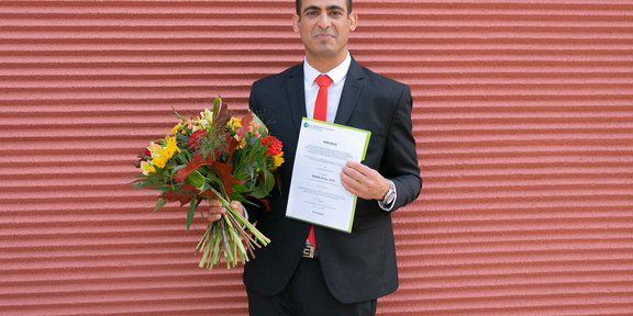 A man holds flowers and a certificate in his hands