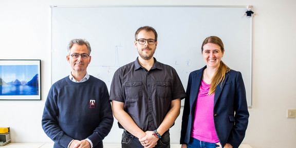 Graduate School of Physics A portrait of two men and a woman in front of a whiteboard with formulas