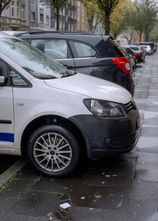 Ein weißes Auto parkt auf dem Bürgersteig neben einem schwarzen Auto.