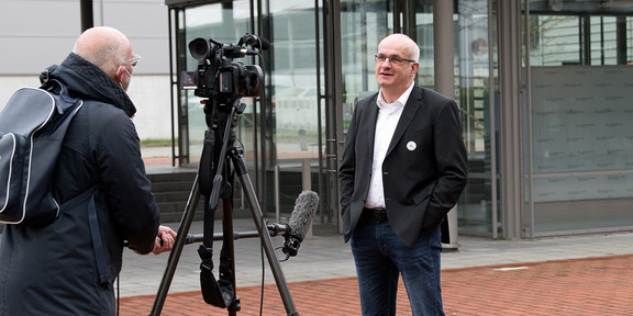 Interview Ein Mann in Anzug steht vor einer Fernsehkamera mit Kameramann.