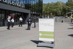 Exam in the Westfalenhalle exhibition center A signpost to the exams stands in front of a large building with a glass front. In Front of the entrance five people are standing in a circle.