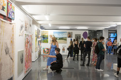 Mehrere Personen stehen in einer Halle einer Kunstausstellung und zwei Personen betrachten ein großes Bild.