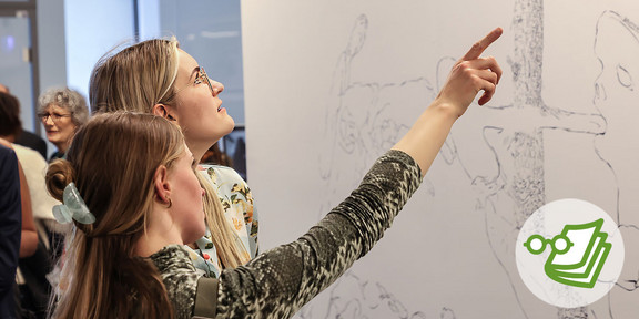 Zwei Frauen, die ein Kunstwerk betrachten. Eine Frau zeigt auf das Kunstwerk.