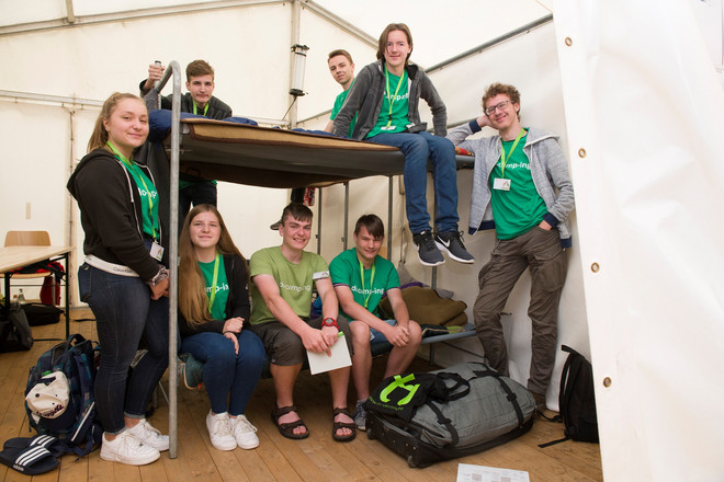 Teilnehmerinnen und Teilnehmer von do-camp-ing posieren in grünen T-shirts um ein Etagenbett