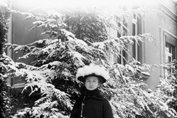 Frau mit langem Mantel vor einem mit Schnee bedecktem Baum
