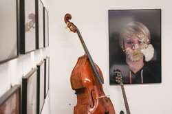 Ein Kontrabass und eine E-Gitarre lehnen in einer Ecke vor einer Wand, an der Porträtfotos hängen.