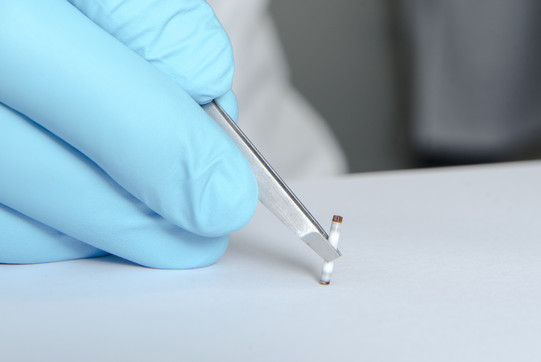 One hand in a blue glove holds a tiny tube with a pipette.