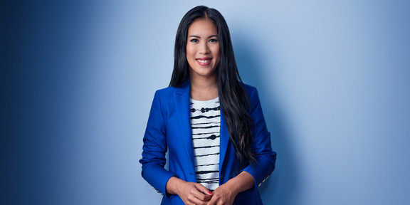 A photo of a smiling woman in a blue blazer and with long, dark hair against a blue background.