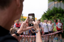 Person filmt mit dem Handy die Starter eines Laufs, die an der Startlinie stehen