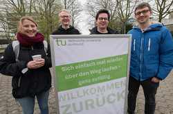 Eine Frau und drei Männer stehen hinter einem Plakat.