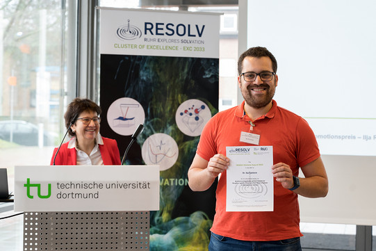 A man with a beard holds up a certificate