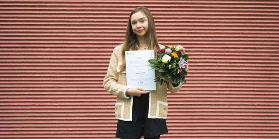 Foto: DAAD-Preisträgerin 2025, Arseniia Mikhailova, hält in der rechten Hand die Urkunde und in der linken einen bunten Blumenstrauß.