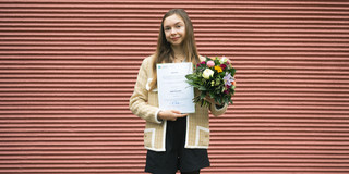 Foto: DAAD-Preisträgerin 2025, Arseniia Mikhailova, hält in der rechten Hand die Urkunde und in der linken einen bunten Blumenstrauß.