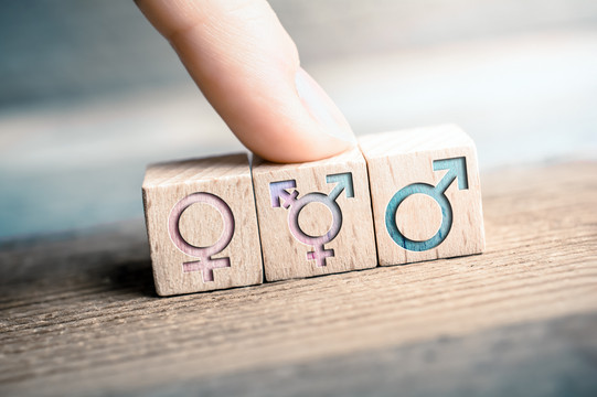 Weibliche, transgender und männliche Icons sind auf 3 Würfeln abgebildet, ein Finger zeigt auf das LGBT-Zeichen.