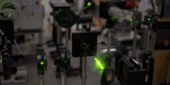 In einem Labor stehen mehrere Geräte und es leuchten grüne Laserstrahlen.