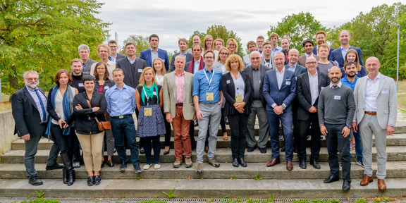 Die Konferenzteilnehmer haben sich zum Gruppenfoto auf einer Treppe versammelt.