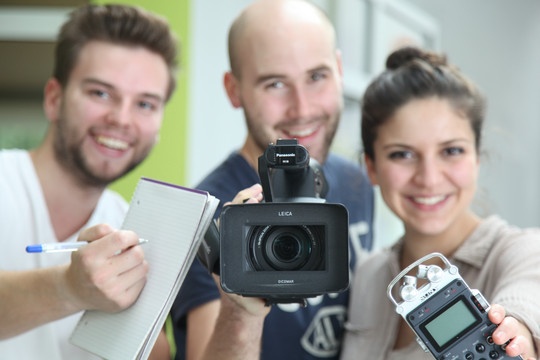 Zwei junge Männer und eine junge Frau mit Notizblock, Videokamera und Audio-Aufnahmegerät