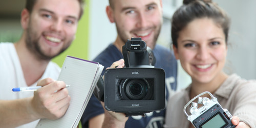 Zwei junge Männer und eine junge Frau mit Notizblock, Videokamera und Audio-Aufnahmegerät