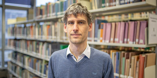 Porträt von Dr. Giulio Mattioli vor einem langen Bücherregal in der Bibliothek