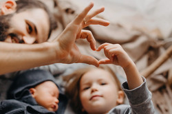 Auf dem Foto sieht man einen Mann, ein Kind und ein Baby. Der Mann und das Kind formen mit ihren Händen gemeinsam ein Herz.