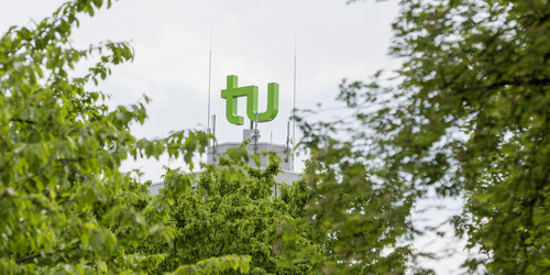 Das grüne TU-Logo umrahmt von Bäumen.