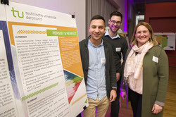 Three people standing next to a poster and smiling at the camera