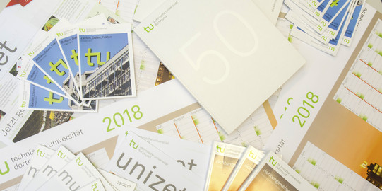 Various folders of TU Dortmund university are lying on a table.