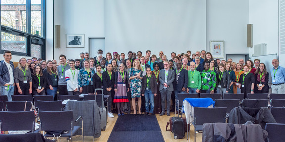 A large group of people is standing in a conference room.