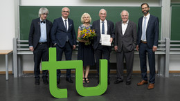Sechs Personen in Anzügen stehen hinter dem grünen TU-Logo vor einer Tafel.