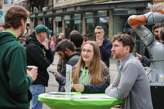 Auf dem Foto sieht man den Infostand der TU Dortmund und mehrere Personen, die sich unterhalten.
