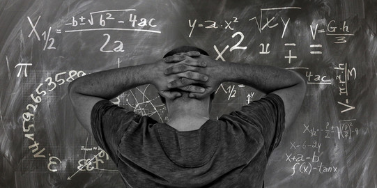 Test anxiety Man crosses arms behind his head while looking at a blackboard with mathematical formulas.