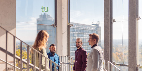 Employees stand in a glass stairwell, Math Tower in the background.