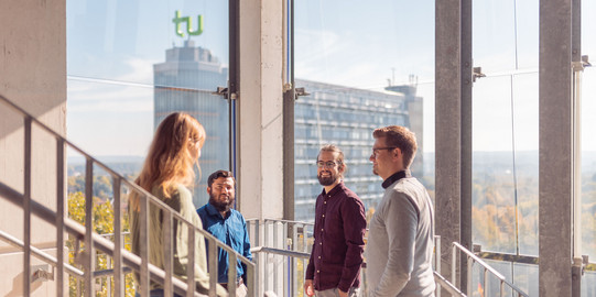 Employees stand in a glass stairwell, Math Tower in the background.
