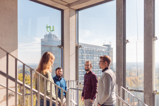 Employees stand in a glass stairwell, Math Tower in the background.
