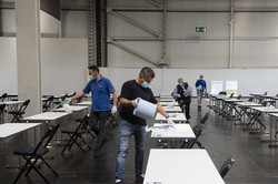 Klausuren in den Westfalenhallen Vier Männer mit Mundschutz reinigen eine Reihe von weißen Tischen mit einer Flüssigkeit und Papiertüchern.