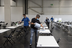 Four men with face masks cleaning a row of white tables with a liquid and paper towels.