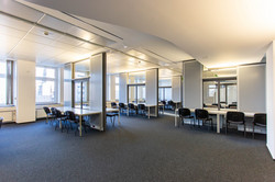 Tables and chairs are placed in an open-plan office in front of partition walls with recessed windows.